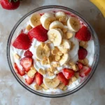 A serving of strawberry banana pudding in a glass bowl with layers of pudding, sliced strawberries, bananas, and vanilla wafers, topped with whipped cream.