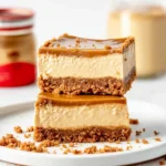 A plate of Biscoff cheesecake bars with a creamy cheesecake layer, buttery crust, and Biscoff topping, garnished with crushed cookies.