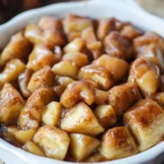 A freshly baked apple cinnamon roll casserole in a baking dish, topped with golden cinnamon rolls and warm spices.