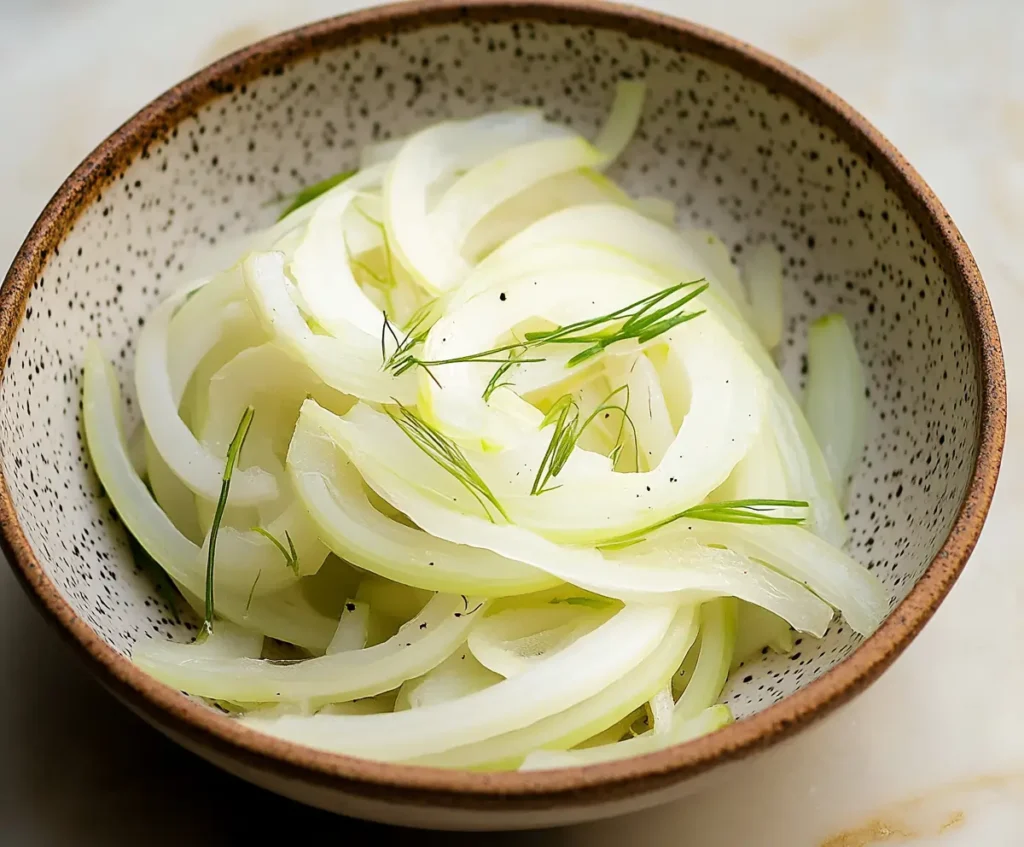 Chopped fennel and onions placed in a speckled white bowl, ready to be added to the Sablefish chowder. The vegetables are sliced thin, with the onion's translucent layers and the fennel's feathery texture clearly visible.